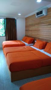 2 Betten in einem Hotelzimmer mit orangefarbener Bettwäsche in der Unterkunft Naura Roomstay in Kuala Tahan