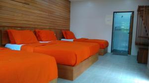 Habitación con 3 camas con sábanas de color naranja y ventana en Naura Roomstay, en Kuala Tahan