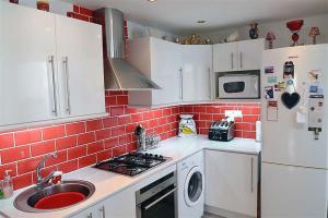 una cocina con armarios blancos y una pared de baldosas rojas en Apartamento Estepona Golf, en Estepona