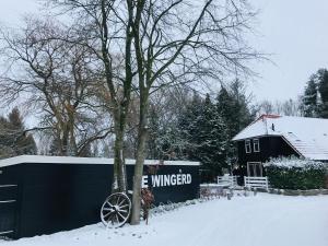 Eine schwarze Scheune im Schnee neben einem Baum in der Unterkunft B&B "de Wingerd" in Bruchterveld