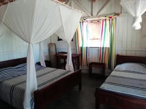 a bedroom with two beds and a window with curtains at Hôtel Safari Vezo Anakao in Anakao