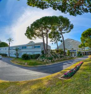 una carretera frente a un edificio con árboles y flores en La Studette Marina 06, en Villeneuve-Loubet
