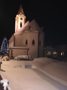 una chiesa con una torre dell'orologio nella neve di notte di Apartmány Grobarčík a Zuberec