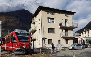 un train rouge se trouve sur la voie en face d'un bâtiment dans l'établissement le stanze del Trenino Rosso, à Tirano