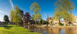 a park next to a river with trees and a building at Fossewold Cotswold Barn in Chipping Campden