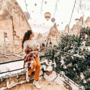 a woman sitting on a ledge looking at a city with hot air balloons at Elite Cave Suites in Goreme
