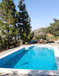 une piscine bleue avec une table, des chaises et des arbres dans l'établissement Hotel B&B Finca la Loma, à Comares
