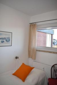 sypialnia z łóżkiem z pomarańczową poduszką i oknem w obiekcie Haus am Deich Wohnung 12 w mieście Dahme