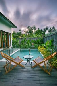 a patio with two chairs and a table next to a pool at The Samara Villas & Restaurant in Ubud