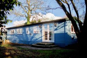 une maison bleue avec une fenêtre et un arbre dans l'établissement Luxurious Rural Cabin with Hot Tub, à West Chiltington