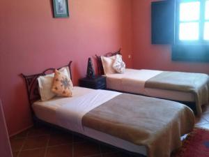 duas camas num quarto com paredes vermelhas em Hôtel La Corniche em Akhfennirr