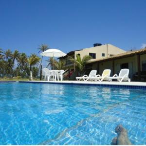 a swimming pool with white chairs and an umbrella at Pousada Aldeia do Forte in Porto de Sauipe