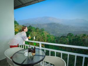 a woman standing on a balcony with a table with a drink at Mistletoe Homestay & Cafe in Munnar