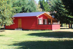 a red cabin with a door in a field of grass at Cabañas Ruta Del Lago in Puerto Varas