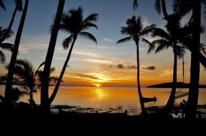 a person sitting in a hammock on the beach at sunset at Coconut Beach Resort in Tavewa