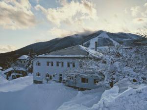 a house covered in snow with a mountain in the background at Raicho Lodge Madarao in Iiyama