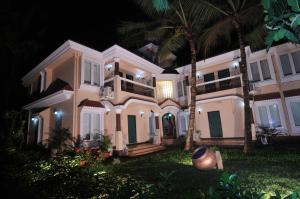 a large white house with palm trees at night at Elegant Shades in Colva