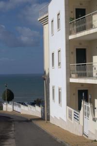 a white building with the ocean in the background at Ericeira Sunset Apartment in Ericeira