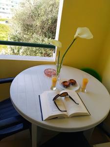 una mesa blanca con un libro y una flor y vasos en Lita Apartment, en Portimão