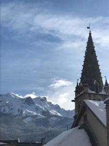a church steeple with snowy mountains in the background at Chez LIZON in Barcelonnette