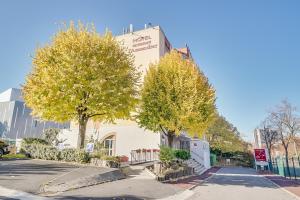 a building with trees in front of a street at Hôtel l'Amandier in Nanterre