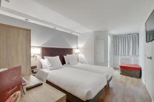 ein Hotelzimmer mit einem großen Bett und einem Schreibtisch in der Unterkunft Hôtel l'Amandier in Nanterre