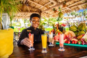 Jewel Paradise Cove Adult Beach Resort & Spa في راناوي باي: امرأة تجلس على طاولة مع أربعة مشروبات