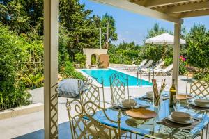 patio ze stołem i krzesłami przy basenie w obiekcie Villa Fanari w mieście Argostoli