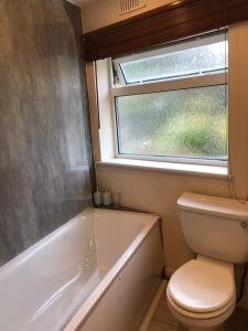 a bathroom with a toilet and a tub and a window at 11 Llainwen Isaf in Llanberis