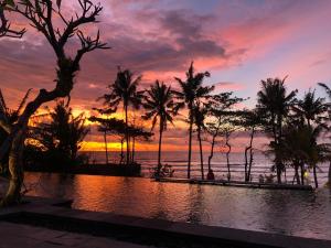 a sunset over the ocean with palm trees and a pool at Bali Natha Beach Front in Canggu