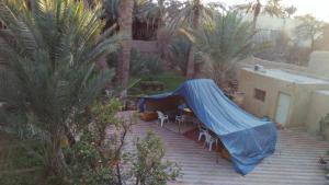 une terrasse avec une bâche bleue au-dessus d'une table et de chaises dans l'établissement gîte les jardins, à Goulmima