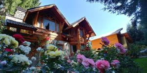 una casa in legno con dei fiori di fronte di ROSALES Alojamiento a Villa La Angostura