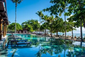 a swimming pool with chairs and palm trees and the ocean at Kûara Hotel in Arraial d'Ajuda