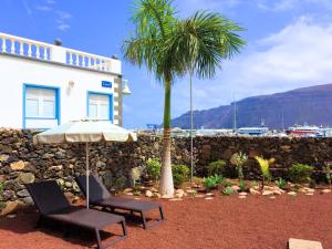 a palm tree and two chairs and an umbrella in front of a building at La Graciosa Magnolia Evita Beach, Frente Mar in Caleta de Sebo
