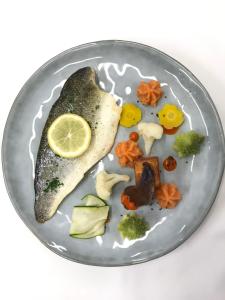 a plate with a fish with a lemon and vegetables at Les Orchidées , Hôtel & Restaurant in Verdun