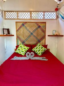 a bedroom with a red bed with green and white pillows at Suba Beach Nipa Huts in Daanbantayan