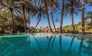 a woman walking by a swimming pool with palm trees at Dev Shree Deogarh in Devgarh