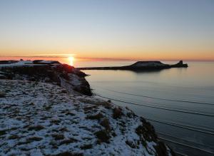 a sunset over a body of water with snow on the shore at King's Head Inn in Llangennith