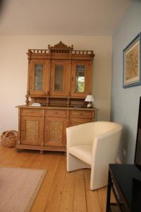 a living room with a wooden cabinet and a white chair at Ferienapartment Alpakas am Schloss in Hamminkeln