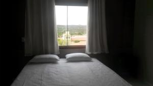 ein Bett mit zwei Kissen in einem Zimmer mit einem Fenster in der Unterkunft Topázio Park Hotel in Afrânio