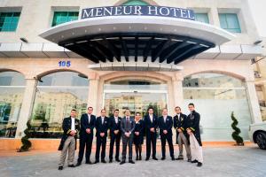 un grupo de hombres con trajes parados frente a un hotel en Meneur Hotel, en Amán