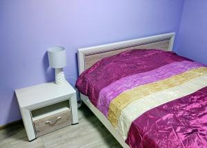 a purple bedroom with a bed and a nightstand with a lamp at Przytulny Apartament w Gołdapi in Gołdap