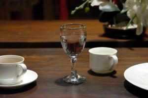 un verre de vin assis à côté de deux tasses sur une table dans l'établissement Puri Langenarjan Guest House, à Yogyakarta