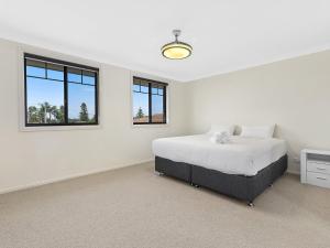 a white bedroom with a bed and two windows at North Entrance Beach House in The Entrance