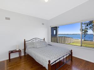a bedroom with a bed and a large window at Lake Edge Cottage in Budgewoi