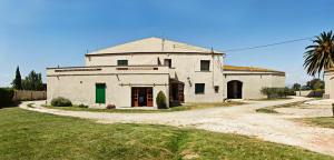 an old white building with a green door on a dirt road at Can Gusó in Castelló d'Empúries