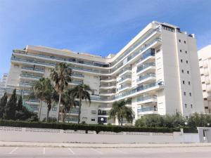 um edifício branco com palmeiras em frente em SALINAS III - PLAYA DE GANDIA ( Sólo alquiler Familias ) em Gandia