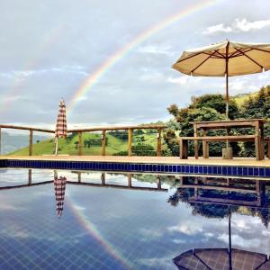 um arco-íris sobre uma piscina com um guarda-sol em Pousada Caminho da Mata em São Bento do Sapucaí