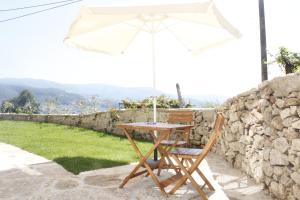 a table and chair with an umbrella on a stone wall at Casa da Nininha in Vale de Cambra