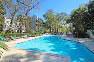 a large blue swimming pool with chairs and trees at Ocean Breeze 23 in Hilton Head Island